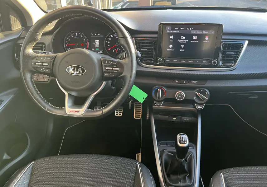 Vue intérieure frontale du poste de conduite de la KIA RIO noire 2021, avec volant multifonction et écran tactile central.