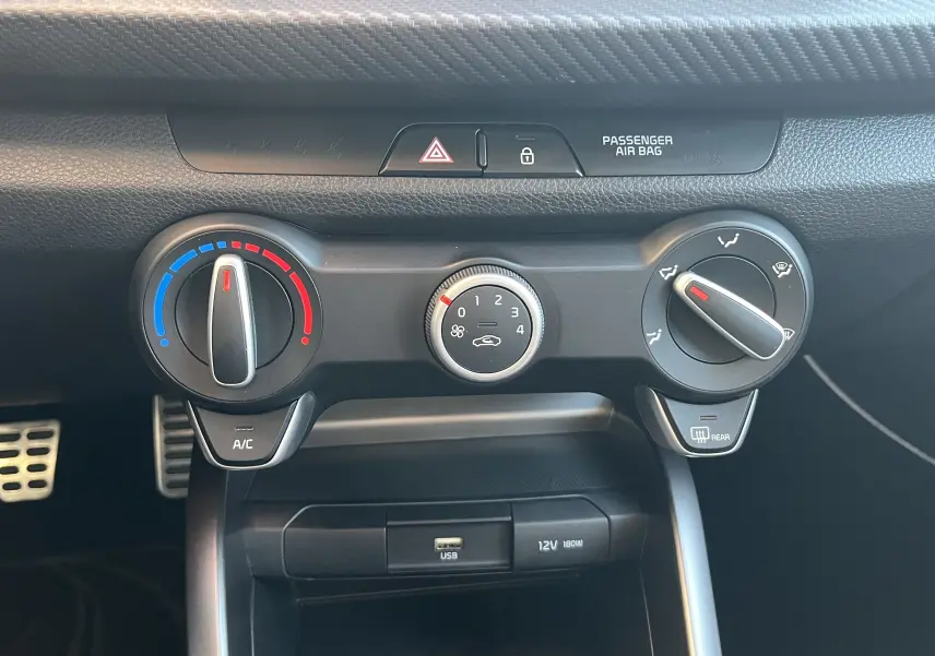 Vue rapprochée des commandes de climatisation et ventilation de la Kia Rio noire, avec réglages manuels et port USB visible.