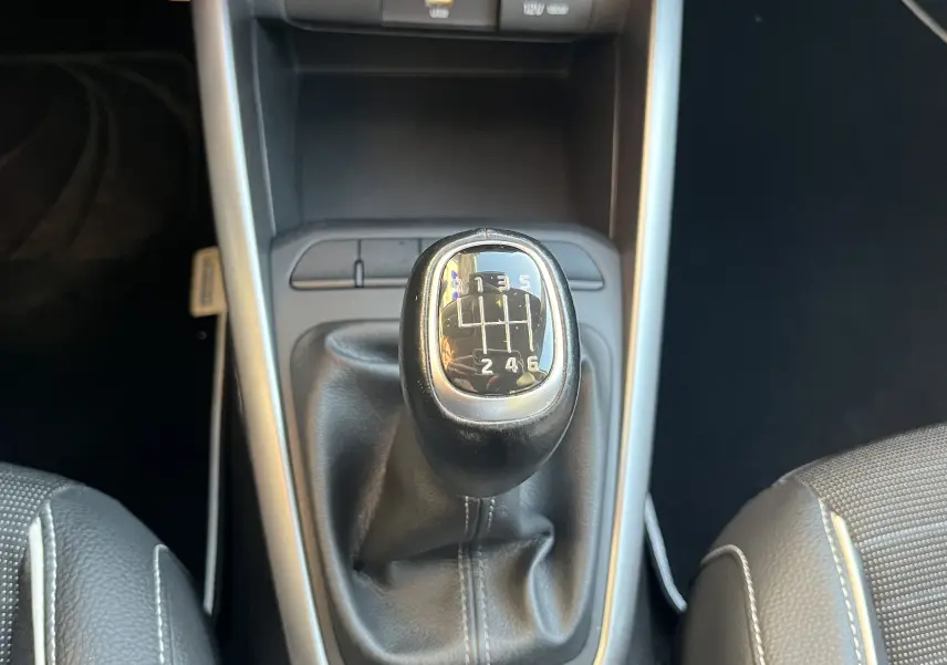 Gros plan sur le levier de vitesse manuel noir de la KIA RIO 1.0 GDI 100 HYBRID GT LINE 2021, entouré de sièges noirs.