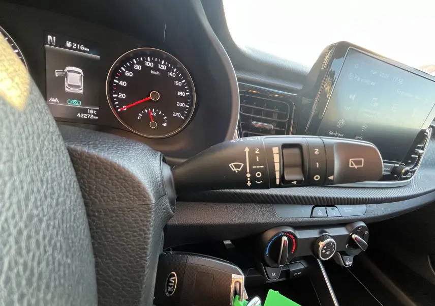 Vue intérieure du tableau de bord de la Kia Rio noire 2021, avec compteur, commandes d’essuie-glace et écran tactile central.