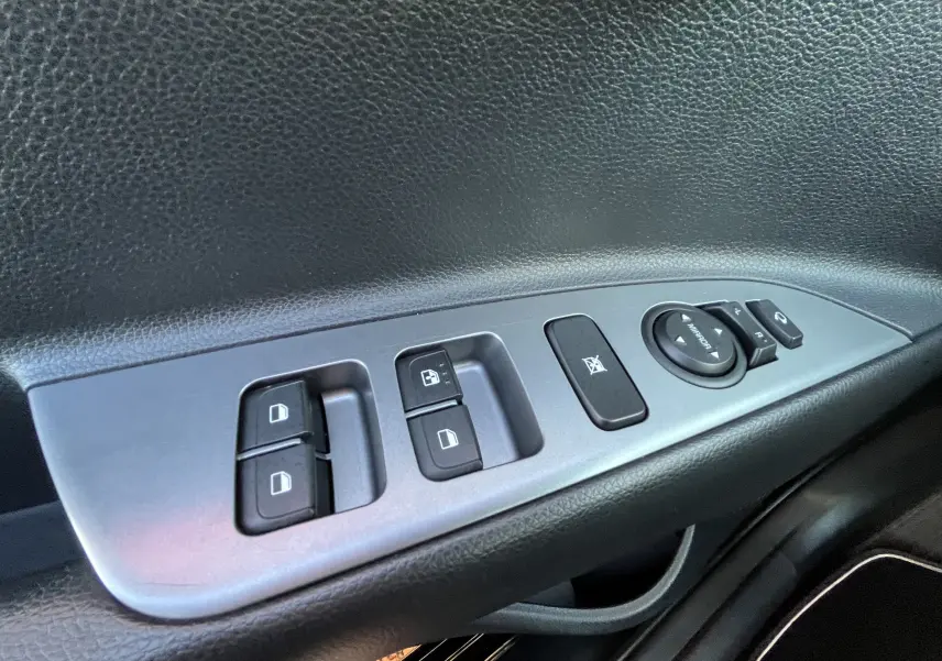 Gros plan sur les commandes de lève-vitres et réglage des rétroviseurs côté conducteur d'une KIA Rio noire 2021.