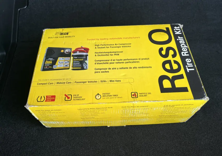 Boîte jaune du kit de réparation de pneus ResQ posée sur un tapis noir, vue en plongée légèrement de côté.