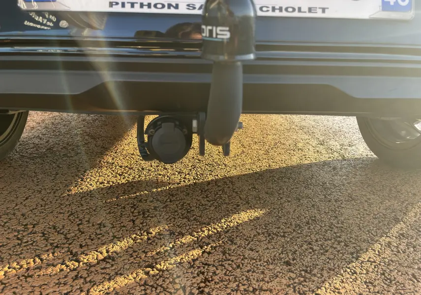 Vue rapprochée de l'attelage noir sous le pare-chocs arrière d'une KIA Rio 2021, avec prise électrique visible.