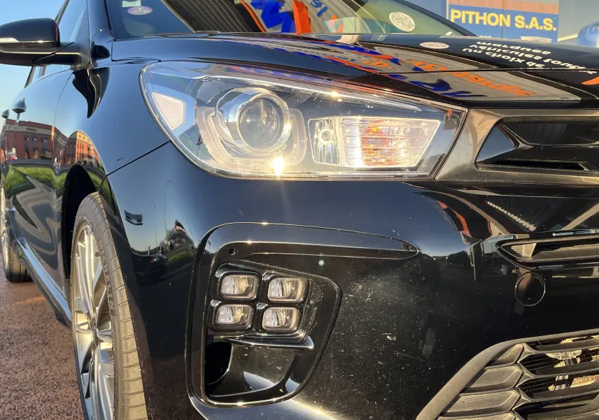 Vue 3/4 avant gauche d'une KIA RIO 1.0 GDI 100 HYBRID GT LINE noire avec phares LED et feux antibrouillard carrés.