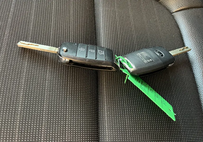 Clé pliable noire de KIA RIO 1.0 GDI 100 HYBRID GT LINE 2021 posée sur un siège en tissu gris foncé à motifs.