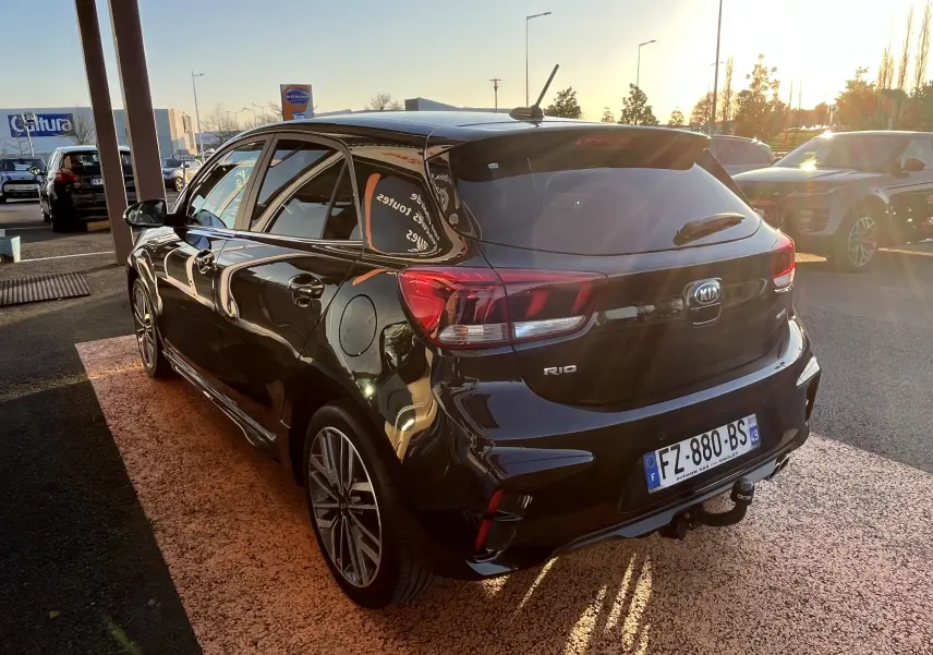 Vue 3/4 arrière droite d'une KIA Rio 1.0 GDI 100 Hybrid GT Line noire de 2021 avec jantes alliage et attelage.