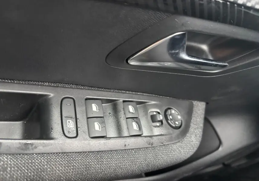 Détail des commandes des vitres électriques et réglages des rétroviseurs sur la portière côté gauche d’une Peugeot 208 gris 2025.
