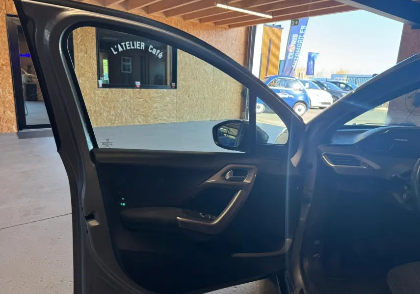 Vue intérieure côté gauche de la porte avant ouverte d’un Peugeot 2008 gris, montrant la garniture et la poignée.