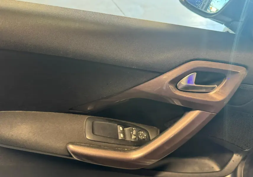 Détail de la porte intérieure côté conducteur du Peugeot 2008 gris, avec commandes des vitres et poignée intégrée.