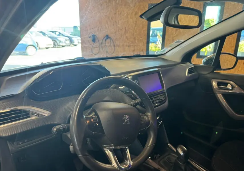 Vue intérieure côté conducteur du Peugeot 2008 gris, montrant le volant, tableau de bord et écran tactile central.