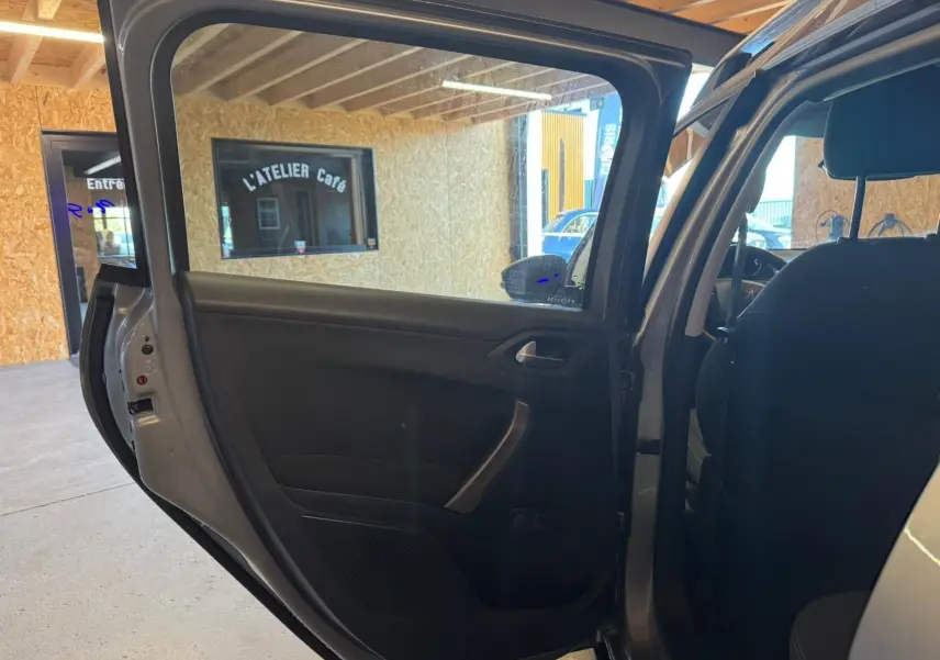 Vue intérieure côté gauche de la porte arrière ouverte d’un Peugeot 2008 gris, montrant la garniture noire et la poignée.