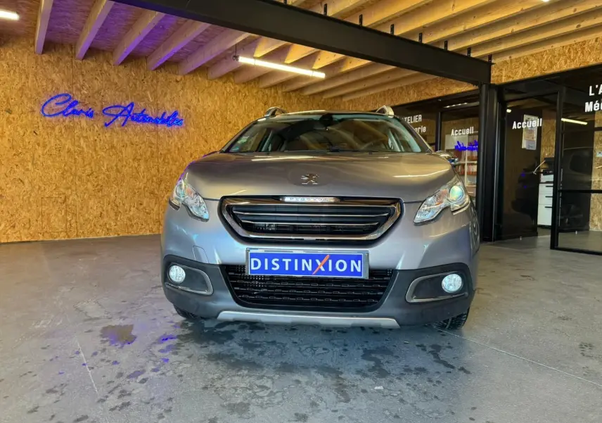 Vue frontale d'un Peugeot 2008 gris 2016 avec calandre noire et plaque d'immatriculation Distinxion dans un showroom.