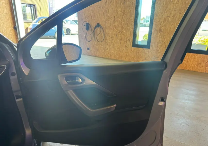 Vue intérieure de la porte avant gauche ouverte d’un Peugeot 2008 gris, mettant en valeur la poignée et les commandes.