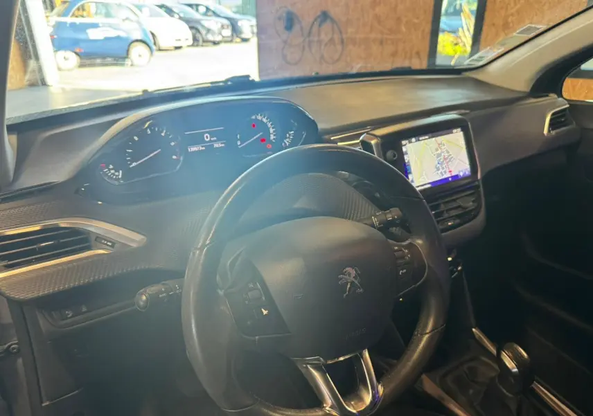 Vue intérieure du poste de conduite du Peugeot 2008 gris, avec volant, tableau de bord digital et écran GPS central.