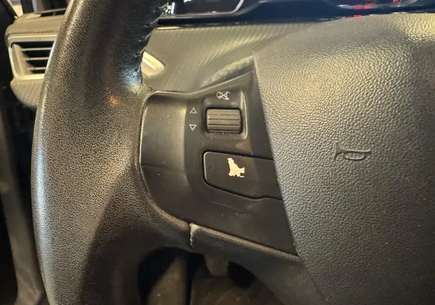 Gros plan sur le volant noir du Peugeot 2008 1.6 HDI 2016, avec commandes audio intégrées à gauche.