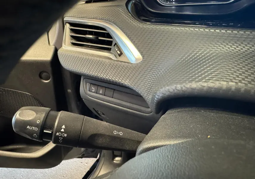 Gros plan sur la manette de clignotants à gauche du volant dans l’habitacle noir du Peugeot 2008 gris 2016.