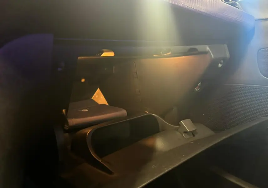 Intérieur du Peugeot 2008 1.6 HDI 100 STYLE 2016 montrant la boîte à gants ouverte avec un livret à l'intérieur, ambiance sombre.