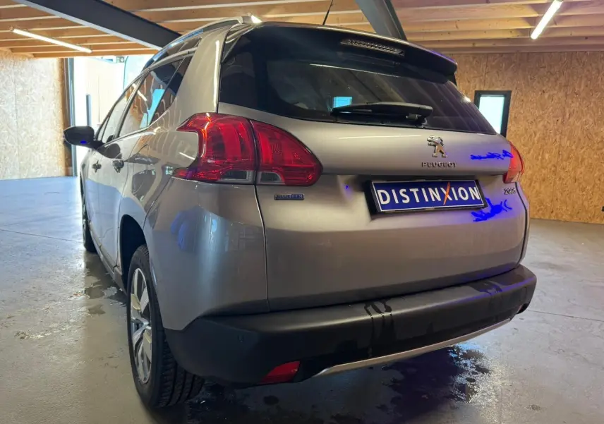 Vue 3/4 arrière droite d'un Peugeot 2008 gris 2016 avec feux arrière rouges et logo distinctif dans un garage.