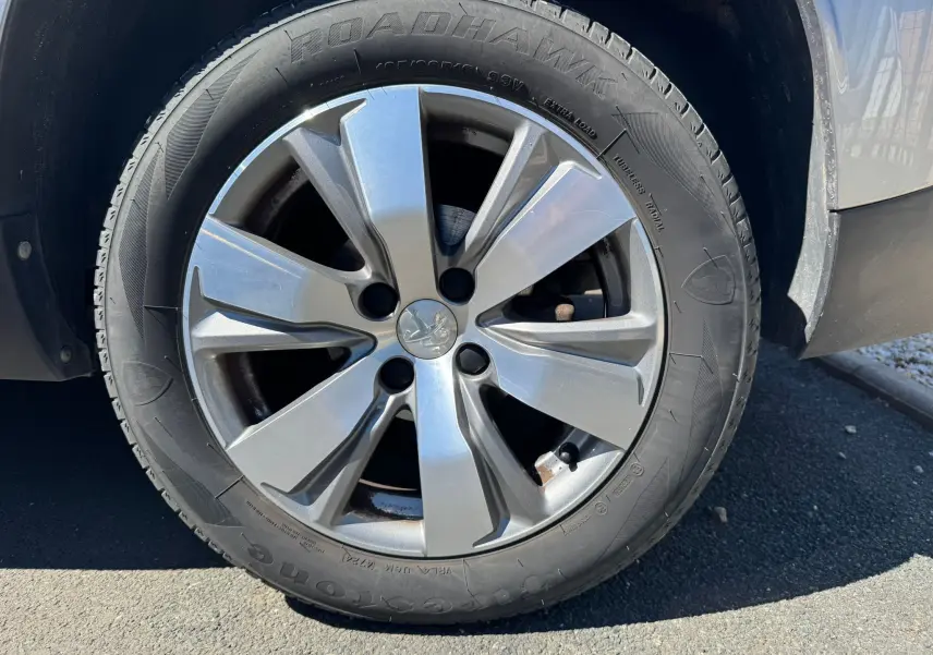 Gros plan sur la roue avant droite d’un Peugeot 2008 gris 2016, mettant en valeur la jante alliage et le pneu Firestone Roadhawk.