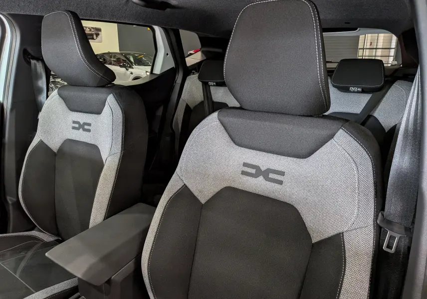 Vue intérieure rapprochée des sièges avant gris et noirs du Dacia Duster Hybrid-G 150 CH 4x4, avec logo distinctif brodé.