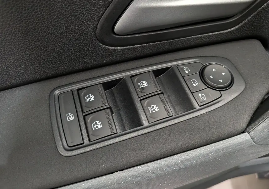 Gros plan sur les commandes des vitres électriques et rétroviseurs sur la porte côté gauche du Dacia Duster Hybrid-G blanc.