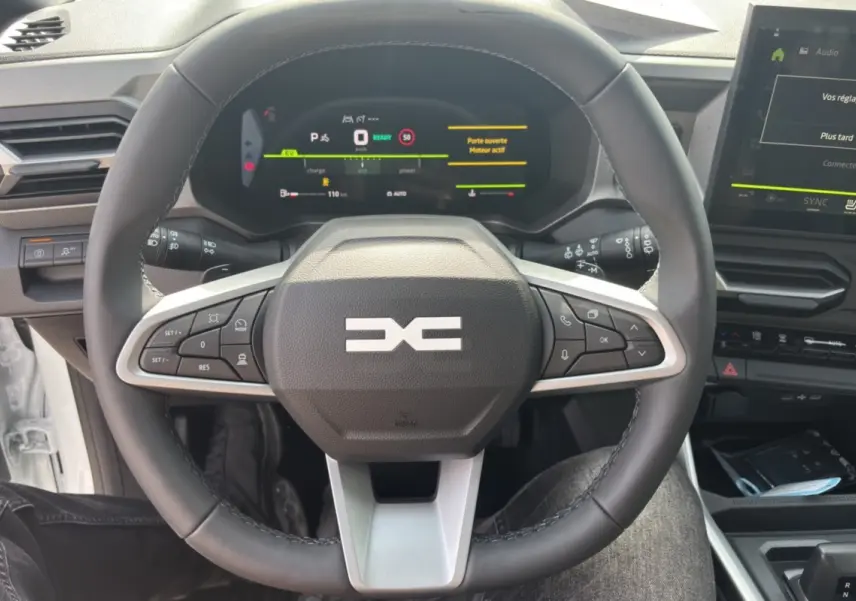 Vue centrée sur le volant cuir du Dacia Bigster Hybrid 150, avec tableau de bord digital et écran tactile visible.