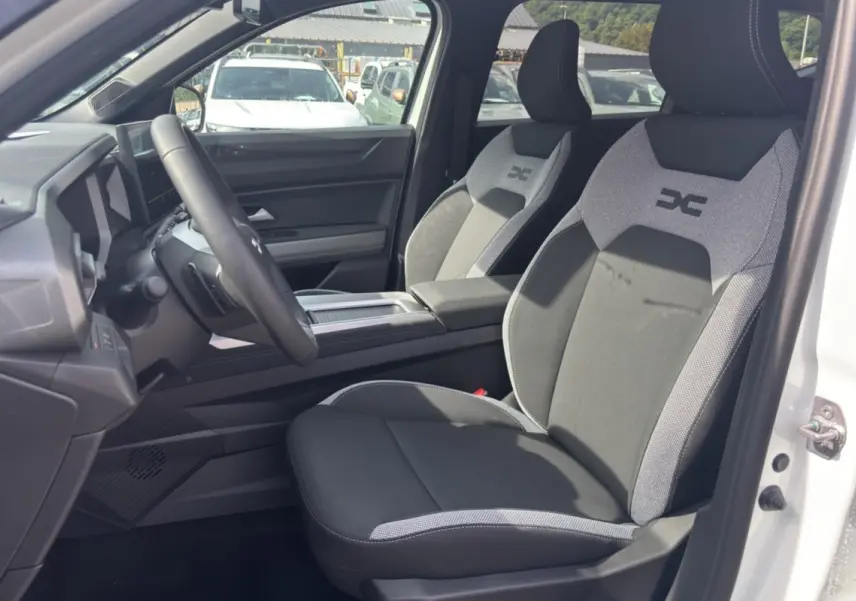 Vue intérieure côté conducteur du Dacia Bigster Hybrid blanc, sièges tissu gris et noir avec logo brodé sur appuie-tête.