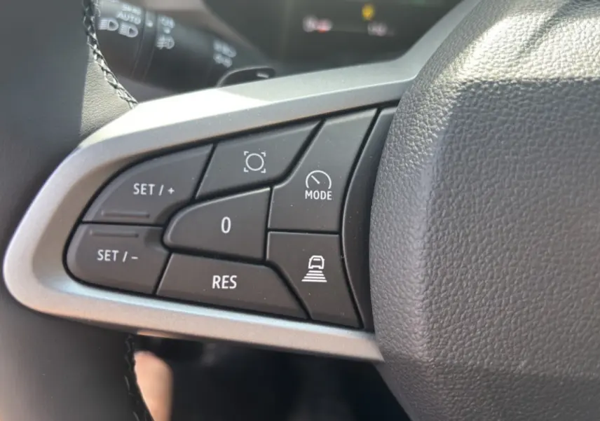 Gros plan sur les commandes au volant cuir du DACIA BIGSTER Hybrid 150, boutons de régulateur et mode conduite visibles.