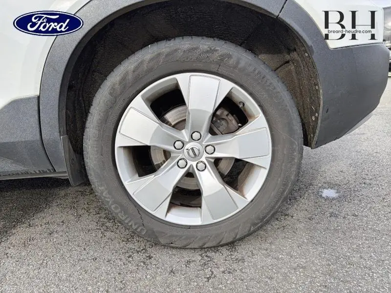 Gros plan sur la roue avant droite d’un Volvo XC40 blanc Glace, mettant en valeur la jante alu à cinq branches.