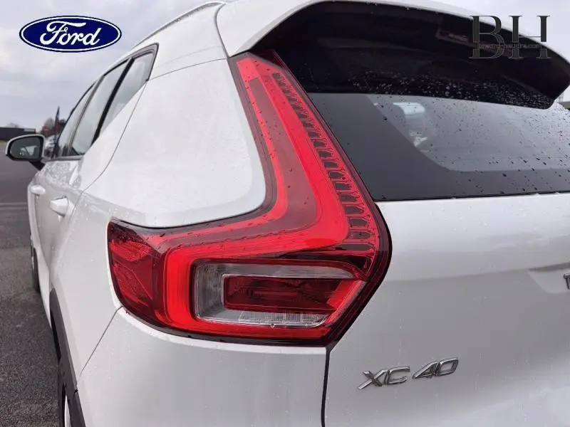 Gros plan sur le feu arrière droit d'un Volvo XC40 blanc Glace sous la pluie, avec logo et badge visibles.