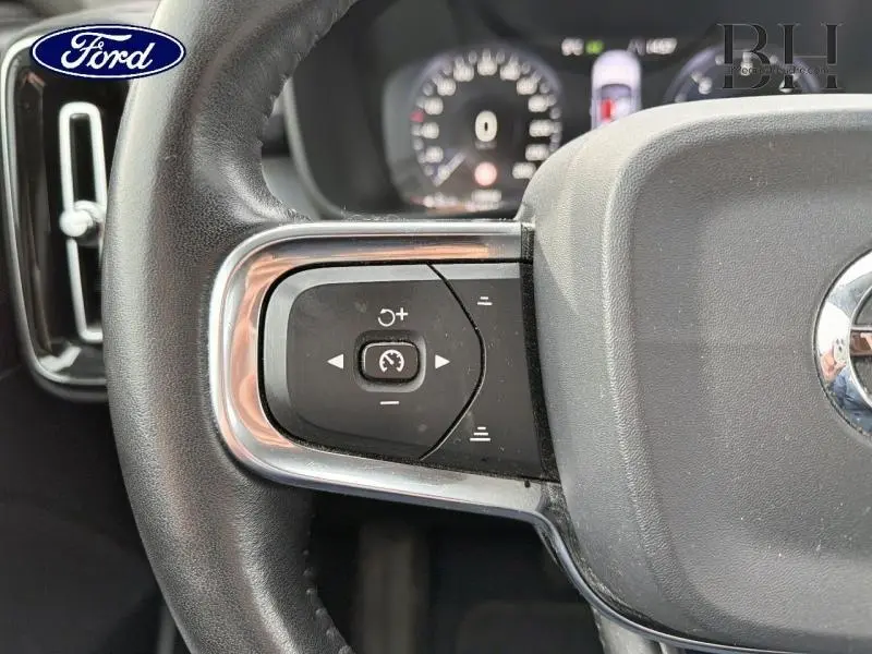 Gros plan sur les commandes de régulateur de vitesse au volant cuir d'un Volvo XC40 blanc Glace, tableau de bord flou en arrière-plan.