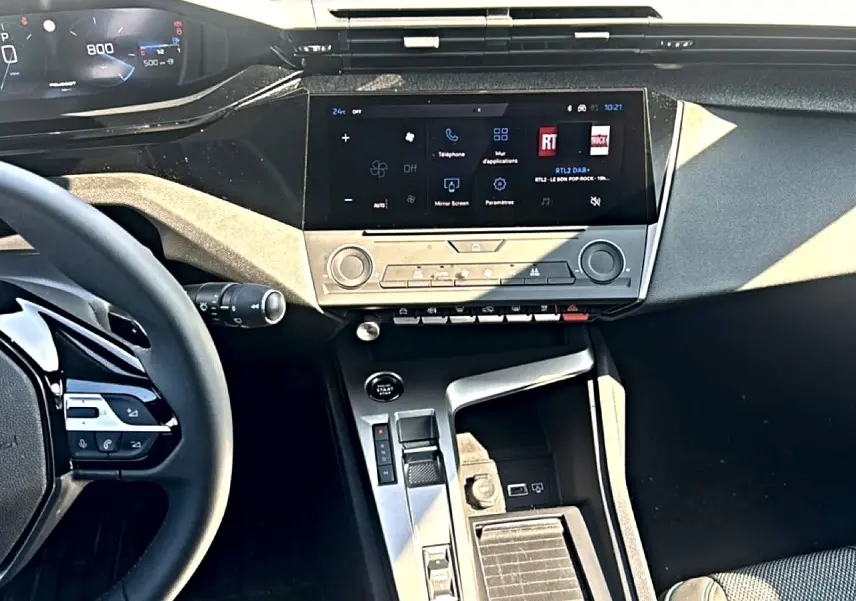 Vue intérieure centrée sur la console centrale et l'écran tactile de la Peugeot 308 2025, volant multifonction visible à gauche.