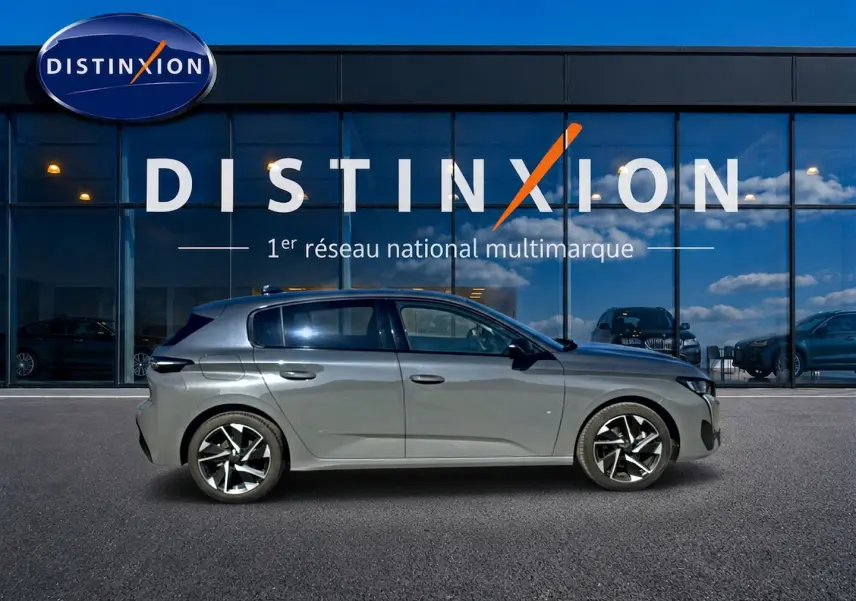Peugeot 308 gris selenium vue de profil côté gauche devant une vitrine avec logo Distinxion.