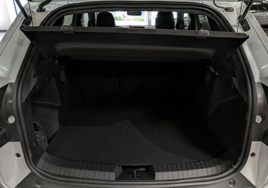 Vue arrière du coffre ouvert du Dacia Duster Hybrid-G blanc glacier, montrant l'espace de chargement vide et la tablette cache-bagages.