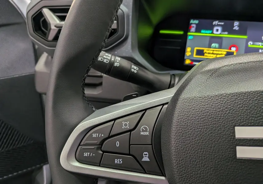 Gros plan sur le volant côté gauche du Dacia Duster Hybrid-G 150 CH 4x4 blanc, avec commandes multifonctions et tableau de bord numérique.