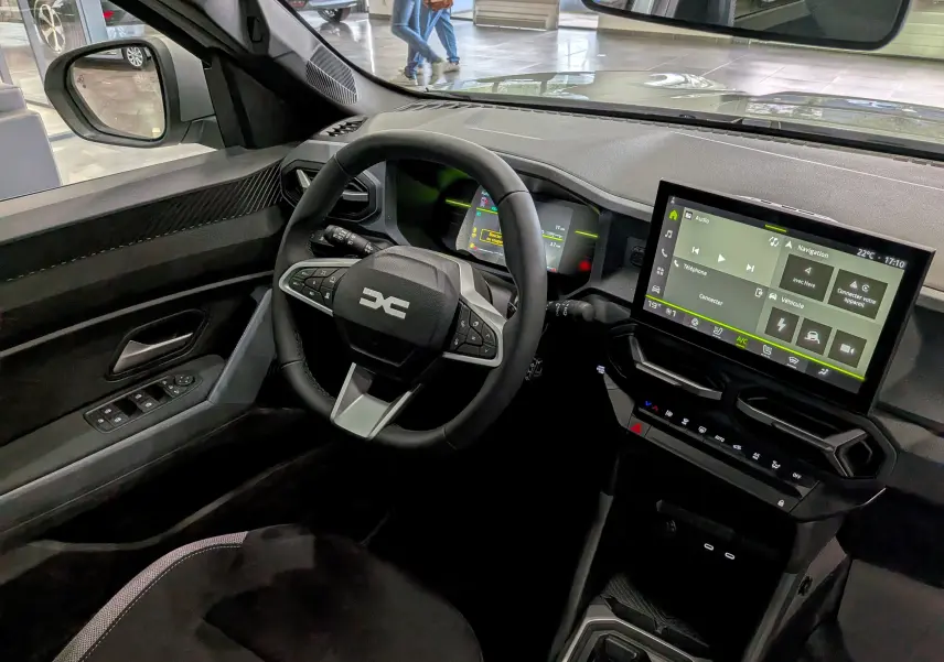 Vue intérieure côté conducteur du Dacia Duster Hybrid-G 150 blanc Glacier, avec tableau de bord numérique et écran tactile central.