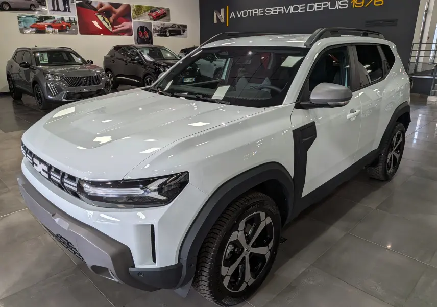 Dacia Duster Hybrid-G blanc glacier en 3/4 avant droit, avec jantes bicolores et détails noirs contrastants.
