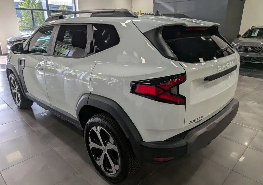 Vue 3/4 arrière droite du Dacia Duster Hybrid-G blanc Glacier, soulignant ses feux arrière et ses jantes bi-ton.