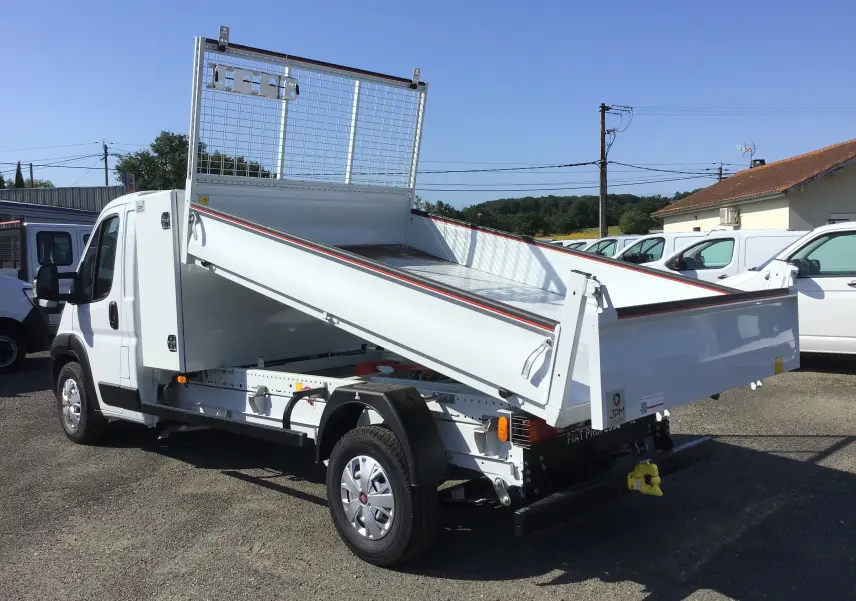 Vue 3/4 arrière droite du FIAT Ducato Chassis Benne blanc 2023 avec benne acier relevée et coffre intégré.