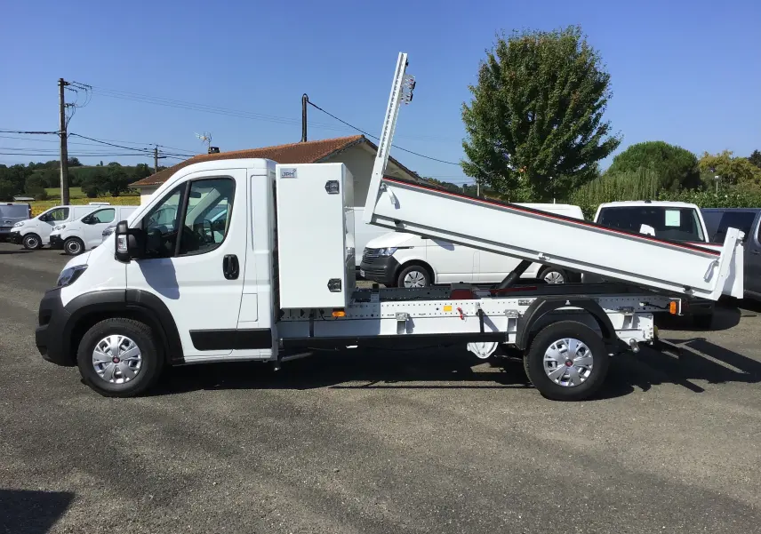 Vue latérale droite d'un FIAT Ducato Chassis Benne blanc 2023 avec benne acier relevée et coffre latéral.