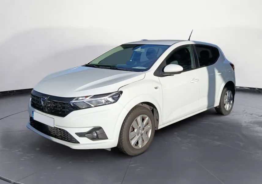 Dacia Sandero blanc vue 3/4 avant droit sur parking gravillonné avec plusieurs véhicules en arrière-plan.