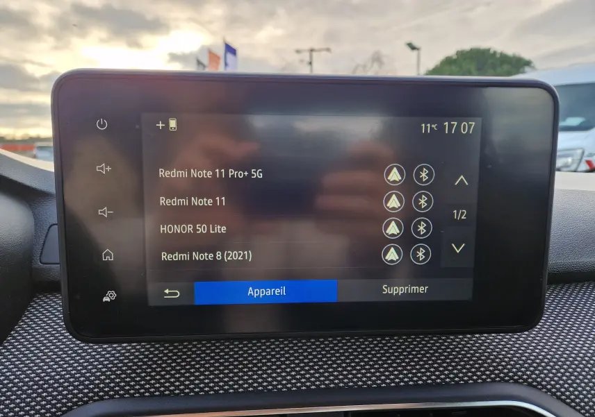 Écran tactile central du tableau de bord d’une Dacia Sandero blanc, affichant la liste des appareils Bluetooth connectés.