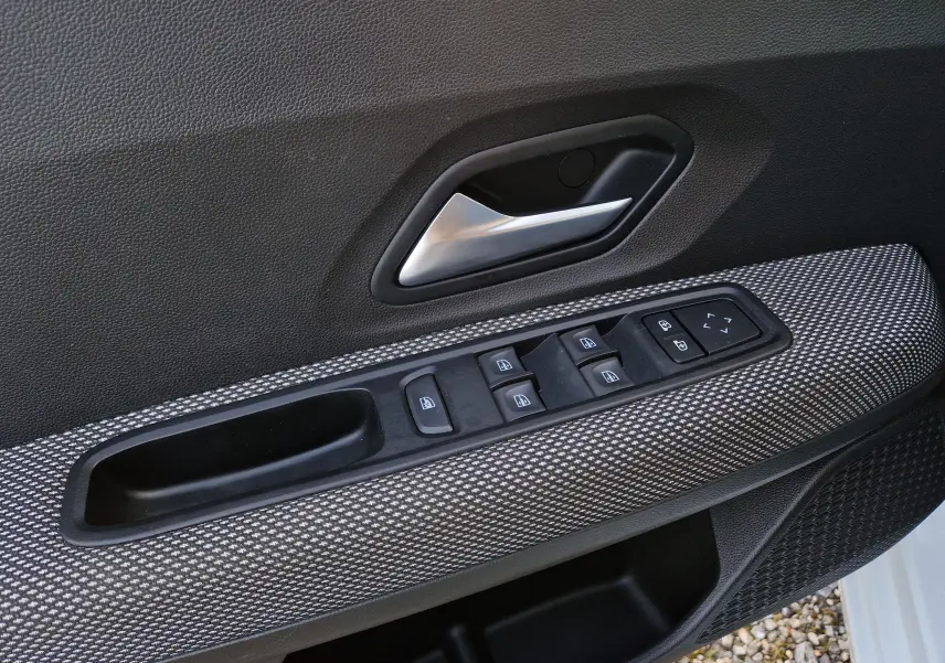 Gros plan sur la commande des vitres et la poignée intérieure côté conducteur d’une Dacia Sandero blanche 2022.