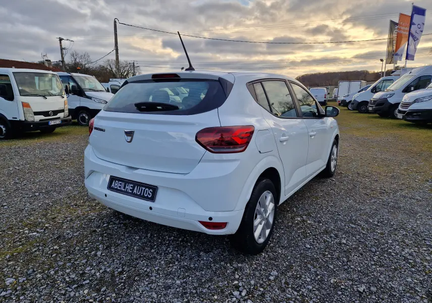 Vue 3/4 arrière droite d'une Dacia Sandero blanche 2022, avec feux arrière LED et antenne de toit visible.
