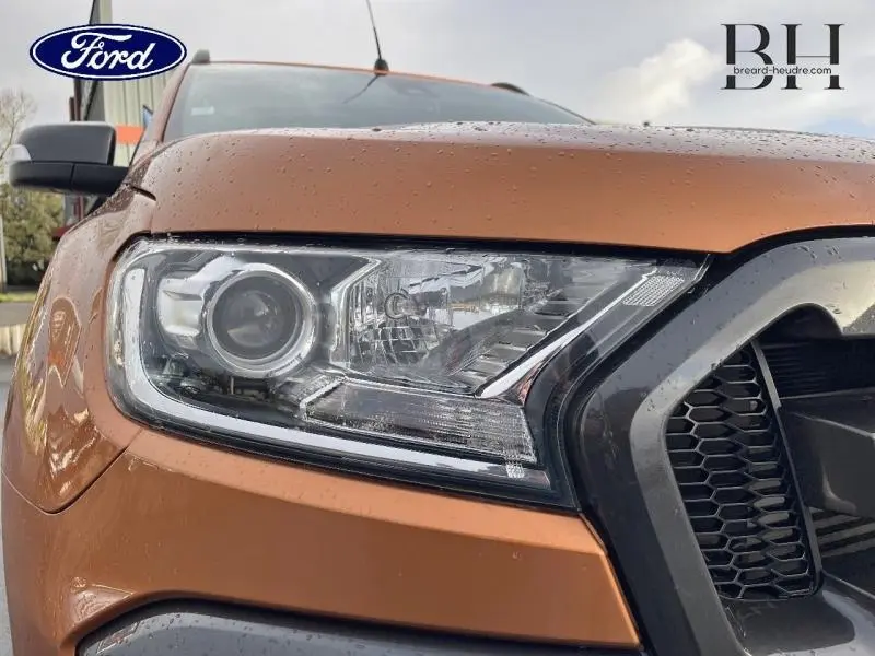 Gros plan sur le phare avant gauche du Ford Ranger Wildtrak 2017 en Pride Orange métallisée avec gouttes de pluie visibles.