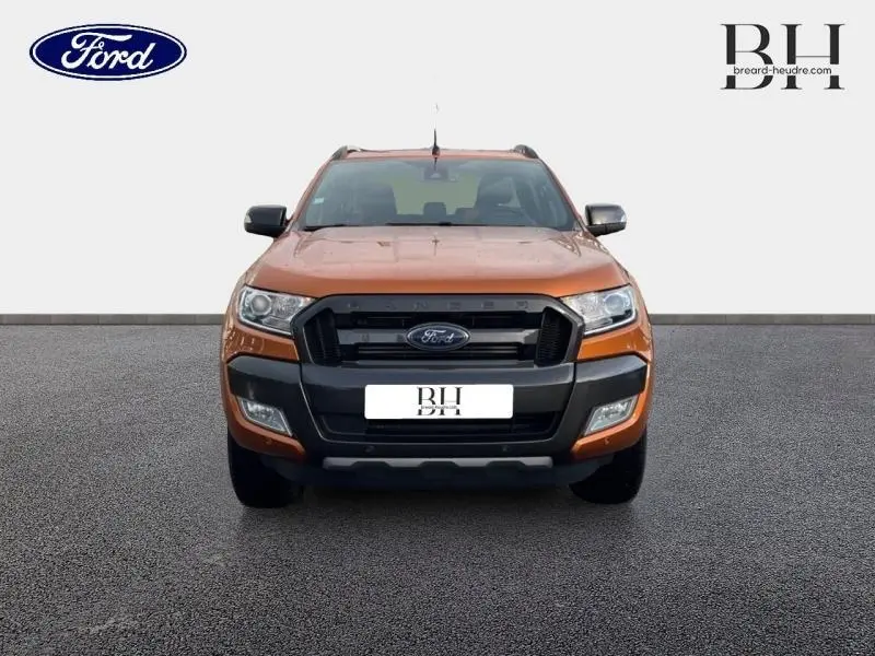 Vue de face du Ford Ranger 3.2 TDCi Wildtrak en orange métallisé avec calandre noire et phares allumés.