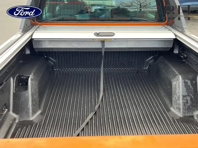 Vue arrière rapprochée du coffre ouvert d’un Ford Ranger Wildtrak Pride Orange métallisée avec plateau rigide noir.
