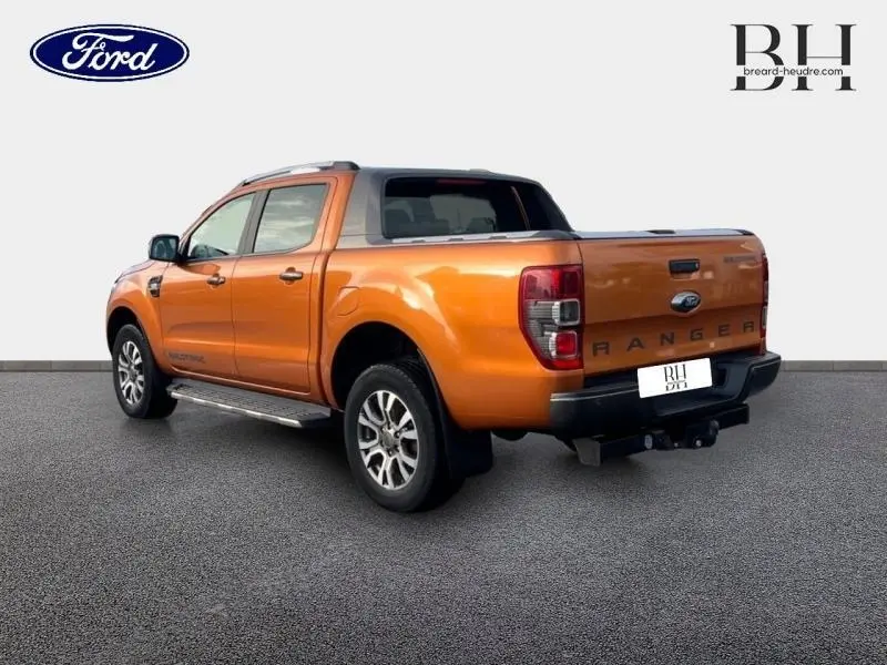 Ford Ranger 3.2 TDCi Wildtrak Pride Orange métallisée vu en 3/4 arrière droit avec rideau de plateau rigide et barres de toit.