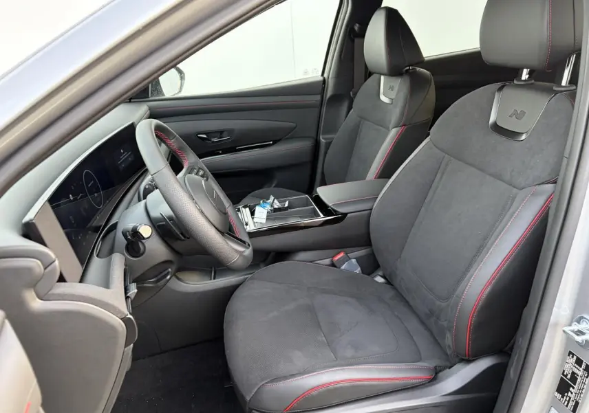 Vue intérieure côté conducteur du Hyundai Tucson 2025, sièges cuir/alcantara noirs avec surpiqûres rouges et volant sport N Line.