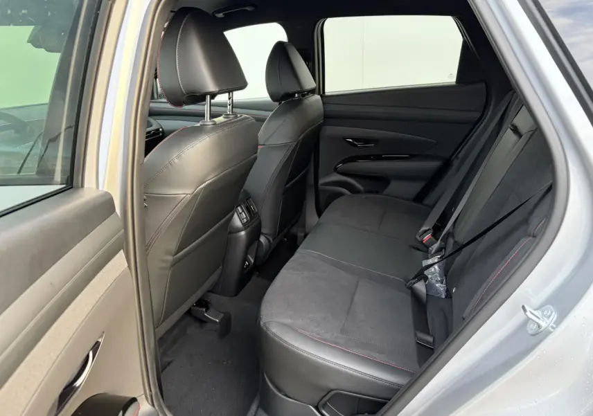 Vue côté droit de l'habitacle arrière du Hyundai Tucson 2025 en Shimmering Silver, sellerie cuir/alcantara noire avec surpiqûres rouges.